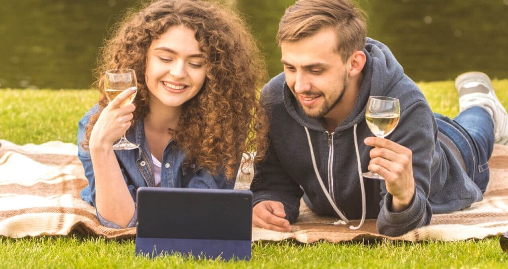 A woman and man laying on a blanket on the grass within a park, looking at an tablet | Consumer behavior