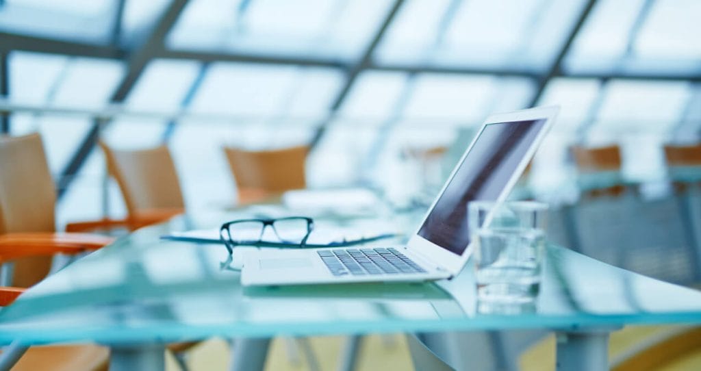 A laptop computer sitting on a glass table with a glass of water and a pair of glass | Ethical data