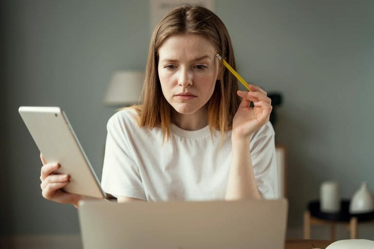 A girl staring at a laptop with a pencil in one hand and a notepad in the other | Website Redesign considerations and what to know in the Perfect Afternoon Morning Show podcast episode