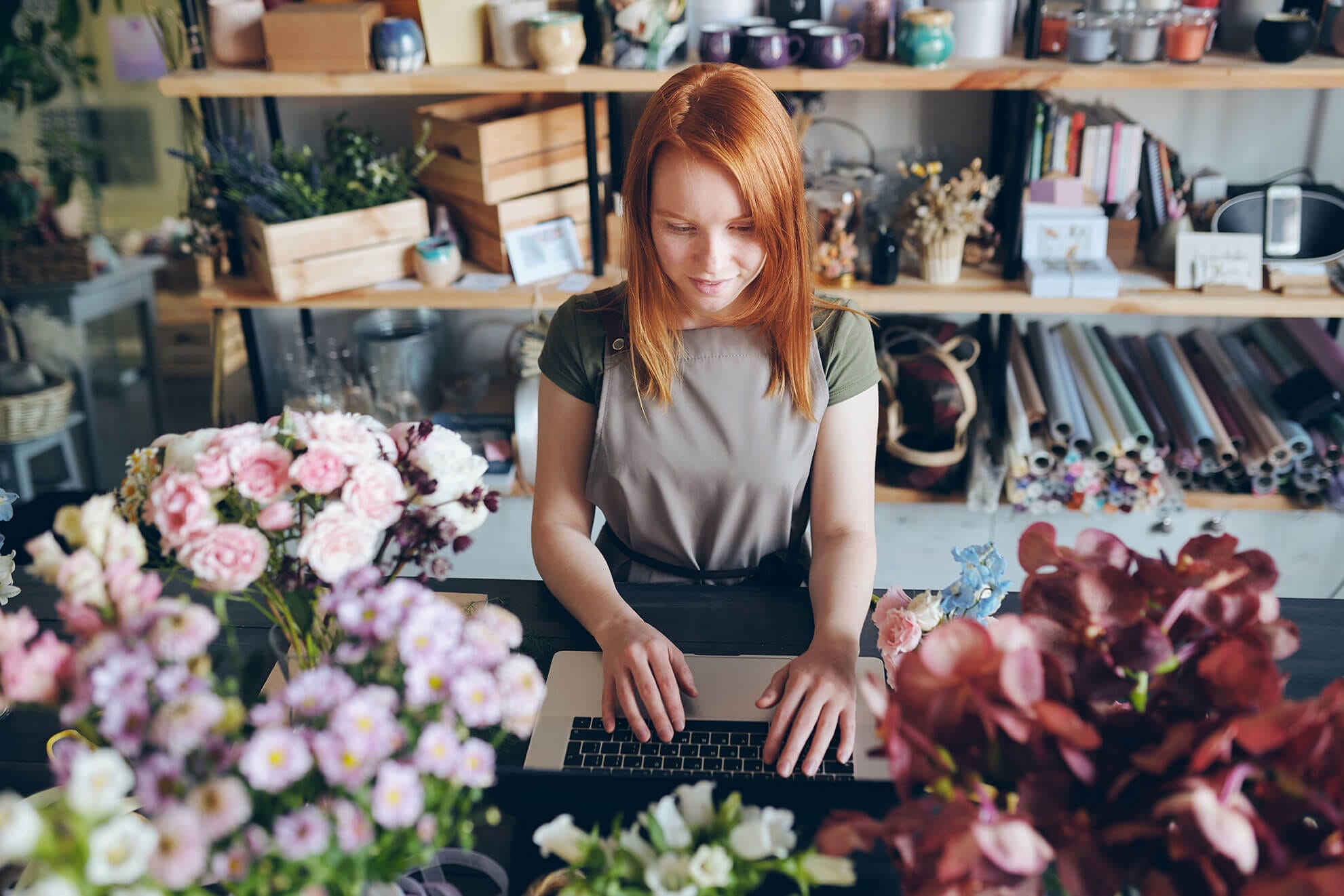 Content redhead florist in apron standing at counter with flowers and working with social media of flower shop | Social Media Audit