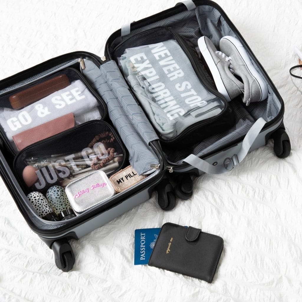 A carry-on suitcase laying on the floor with Miamica packing cubes, pill case, and passport covers.